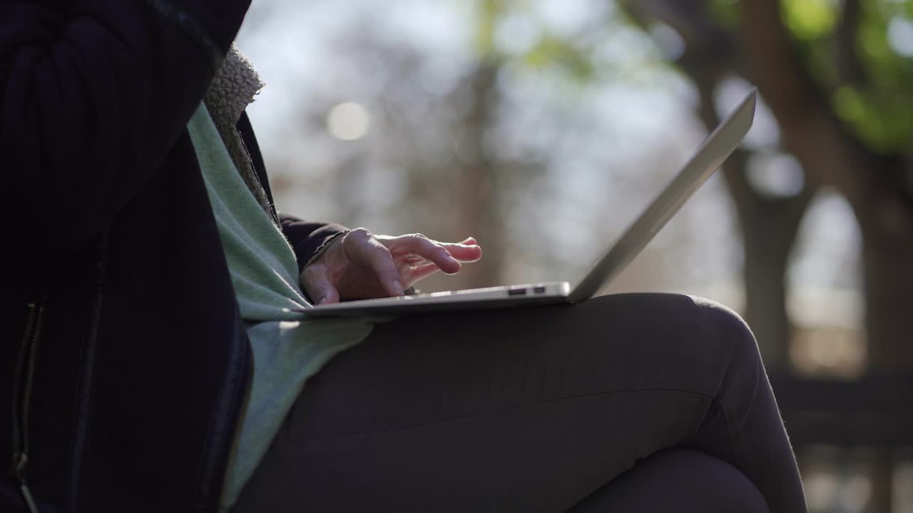 Cropped shot of woman sitting on wooden bench with laptop