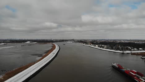 industrial ship with containers sailing on serene noord river under cloudscape during winter in south holland, netherlands. - aerial wide shot