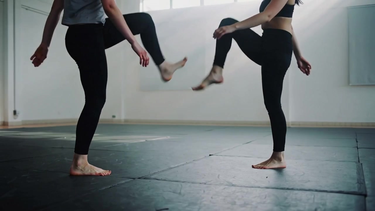 Cueing women dancers lifting knees, stepping on mat by windows, training in sports bra, leggings