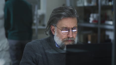 mature man with beard and glasses working on computer in a dim room