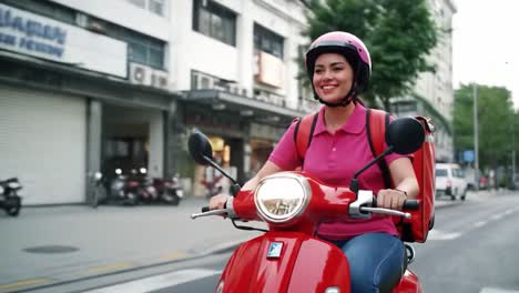a delivery rider wearing a pink helmet and uniform glides smoothly through bustling urban streets, spreading joy while making deliveries on a red scooter under clear skies.