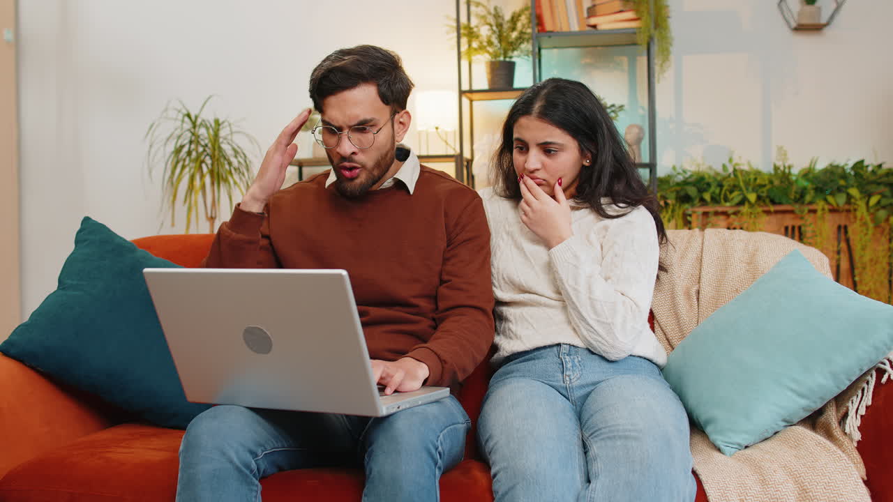 conmocionado decepcionado joven pareja de familia india usando portátil leyendo malas noticias desafortunadas fracasan pierden