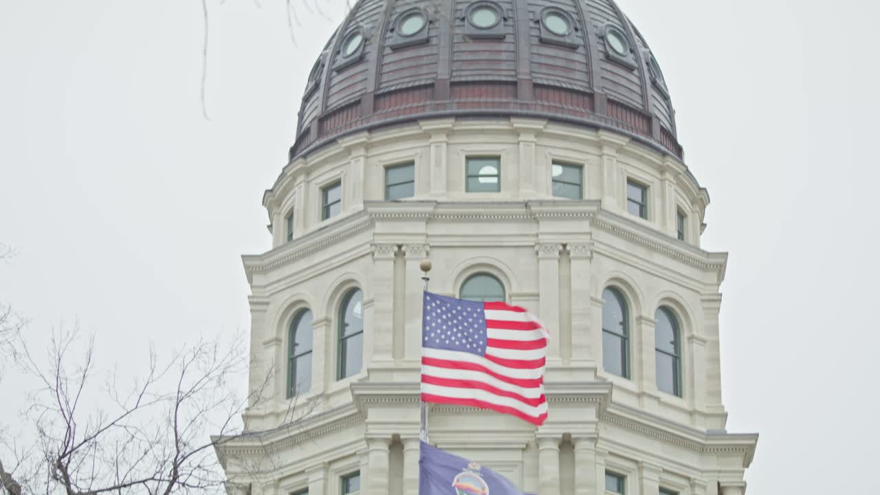 edificio del capitolio del estado de kansas con banderas ondeando en topeka, kansas con video de primer plano inclinándose hacia abajo