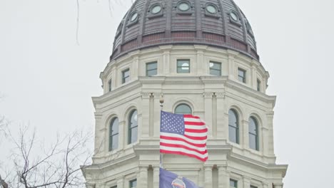 Edificio-Del-Capitolio-Del-Estado-De-Kansas-Con-Banderas-Ondeando-En-Topeka,-Kansas-Con-Video-De-Primer-Plano-Inclinado-Hacia-Abajo