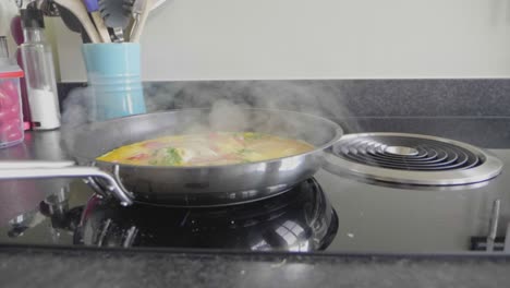 panning shot of an omelet with cheese and vegetables baking in a skillet