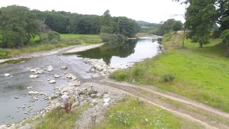 Drone-footage-flying-low-and-slowly-over-a-shallow,-calm-river-and-vehicles-crossing-point-and-track-in-the-Lake-District,-UK