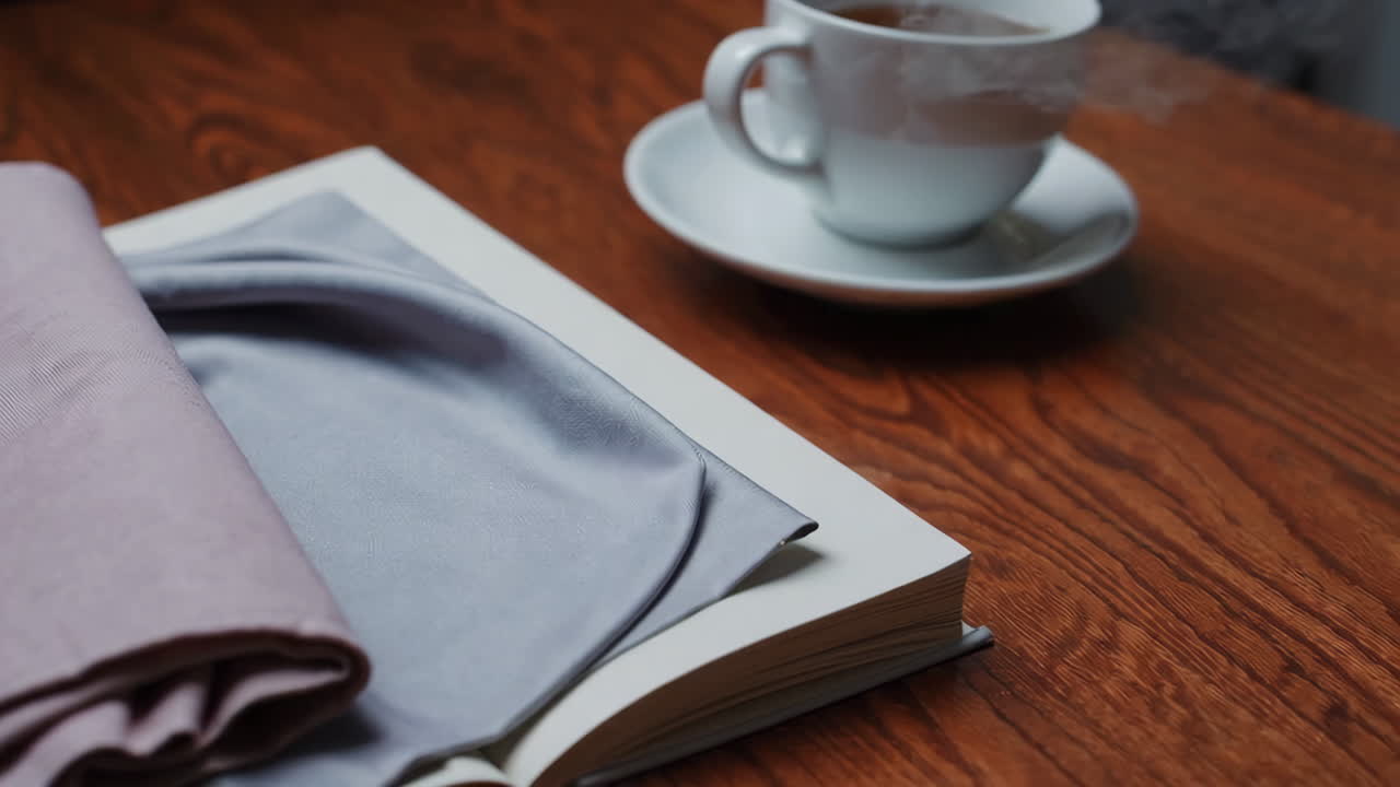 Livro aberto, xícara de chá e tecido em mesa de madeira