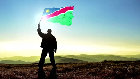 hombre de silueta exitoso ganador agitando la bandera de namibia en la cima de la montaña, fondo de bucle de cinemagraph