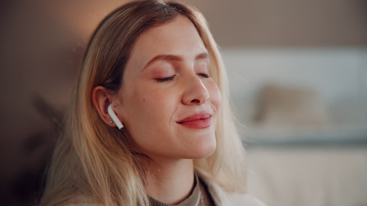 A beautiful blonde woman smiles while wearing white earbuds.