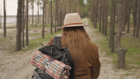 una irreconocible campista pelirroja aventurera caminando a través de los árboles de un bosque 1