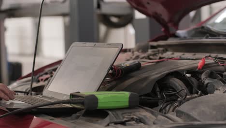 computer diagnostics of cars, young mechanic specialist male uses laptop technology while repairing vehicle with open hood at service station