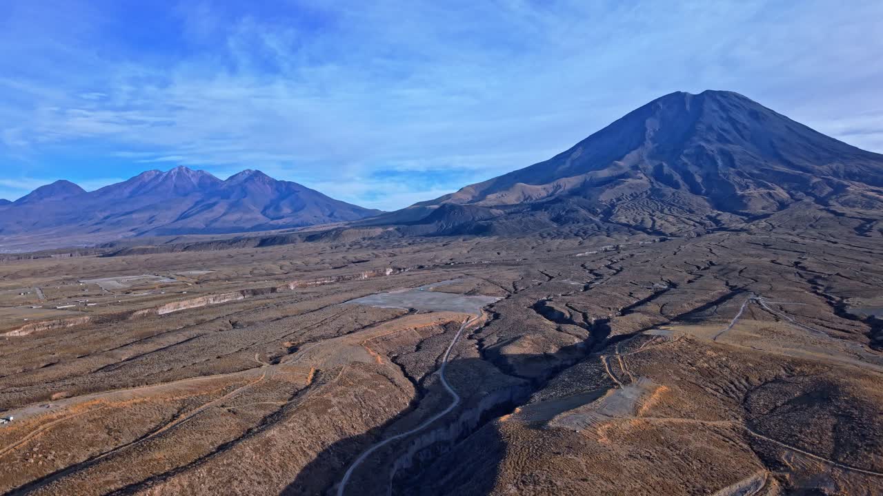 Ripresa aerea ascendente che cattura il Misti e l'imponente picco del Chachani, illuminati dalla calda luce dorata dell'alba, evidenziando i pendii vulcanici e il paesaggio aspro delle Ande sotto un glorioso cielo mattutino.