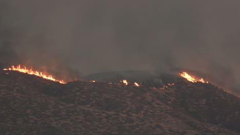 pan of plane flying in dark smoke over wildfire on hills in california