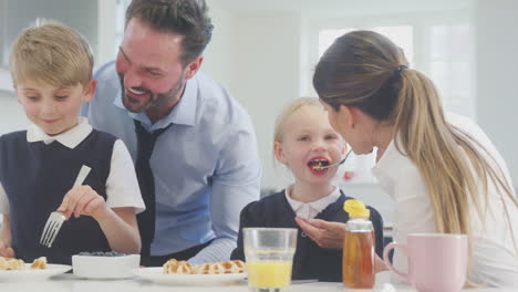 Kinder-In-Schuluniform-Stehen-In-Der-Küche-Und-Essen-Frühstückswaffeln,-Während-Sich-Die-Eltern-Auf-Die-Arbeit-Vorbereiten