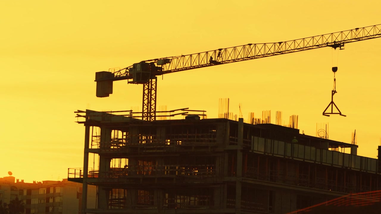 Tower crane lifts building materials at a construction site during sunset