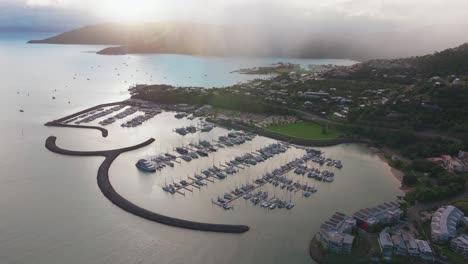 Port-Airlie-Beach-Bay-Lagoon-Coral-Sea-marina-jetty-yachts-sailboats-aerial-drone-cloud-layer-mist-sunrise-morning-rain-clouds-heart-of-Great-Barrier-Reef-Whitsundays-Whitehaven-forward-pan-up-reveal