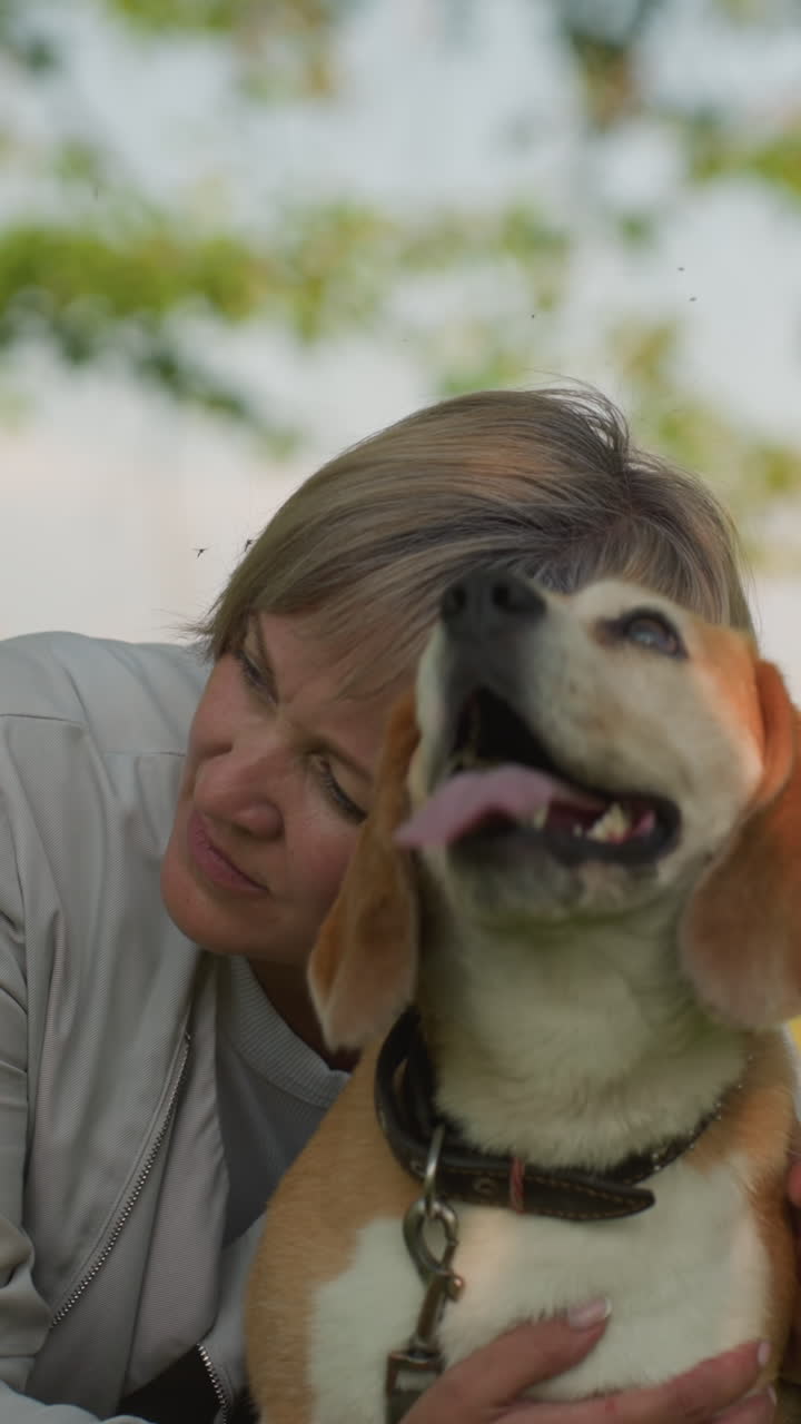 mujer sentada en un campo de hierba sosteniendo a su perro con afecto, acariciando suavemente y descansando la cabeza sobre el perro, creando un momento conmovedor de calor y amor, el fondo presenta vegetación exuberante y árboles