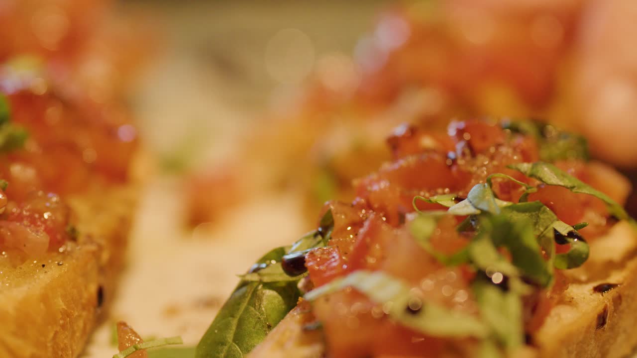 Warm lighting highlights bruschetta topped with tomato, basil, and balsamic glaze in shallow focus