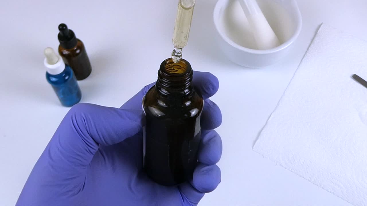 Laboratory technician formulating a cosmetic serum by adding drops to an amber bottle