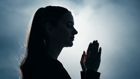 woman praying silhouetted against the sky