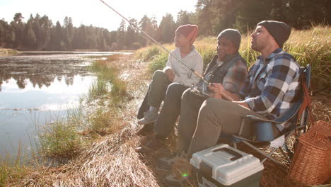 Grandfather,-father-and-son-sit-fishing-by-a-rural-lake