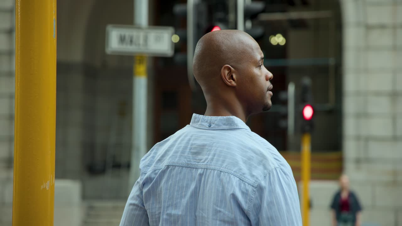 Man in light blue shirt standing at curb, scanning intersection and responding to red signal