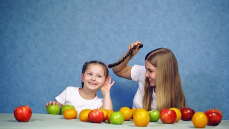 girls at table with fruit. woman having fun with girl at table with fruit