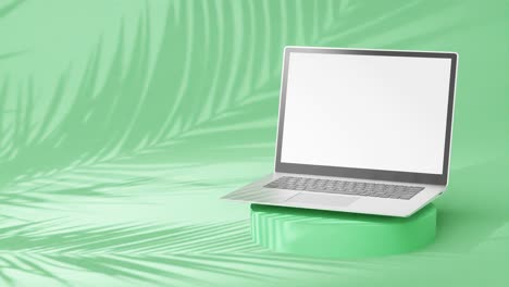 Sleek-silver-laptop-on-round-pedestal,-empty-screen-with-palm-tree-shadows-on-green-background