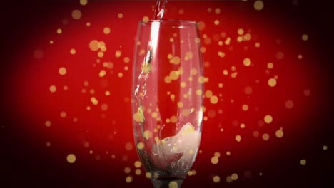 Yellow-spots-floating-over-drink-pouring-into-champagne-glass-against-red-background