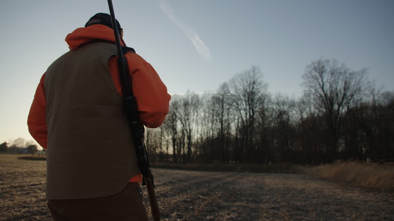 Hunter Walks Through Field At Sunset With Rifle Slow Motion