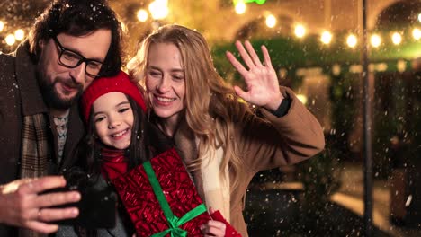 vista de cerca de una familia feliz caucásica sosteniendo regalos y haciéndose un selfie mientras nieva en navidad