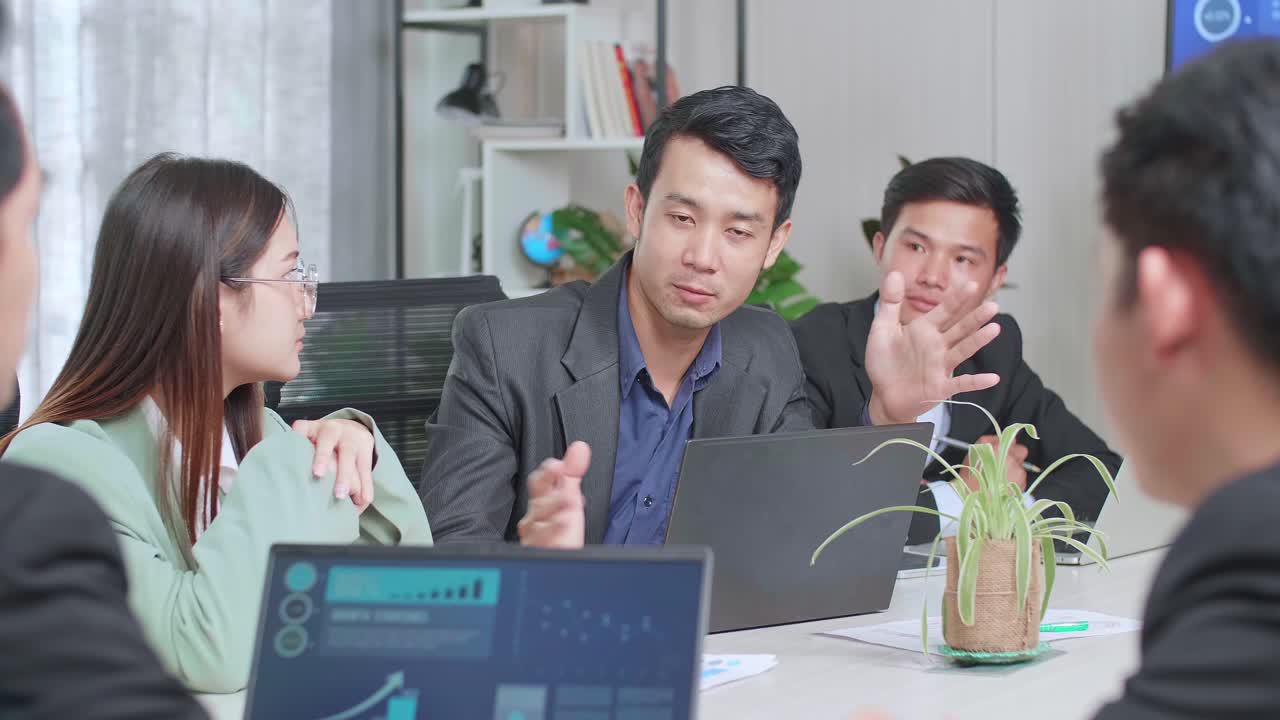 Young Asian Team Have Meeting In A Conference Room. They Share Opinions, Statistics Show On Laptop Computer And Tv