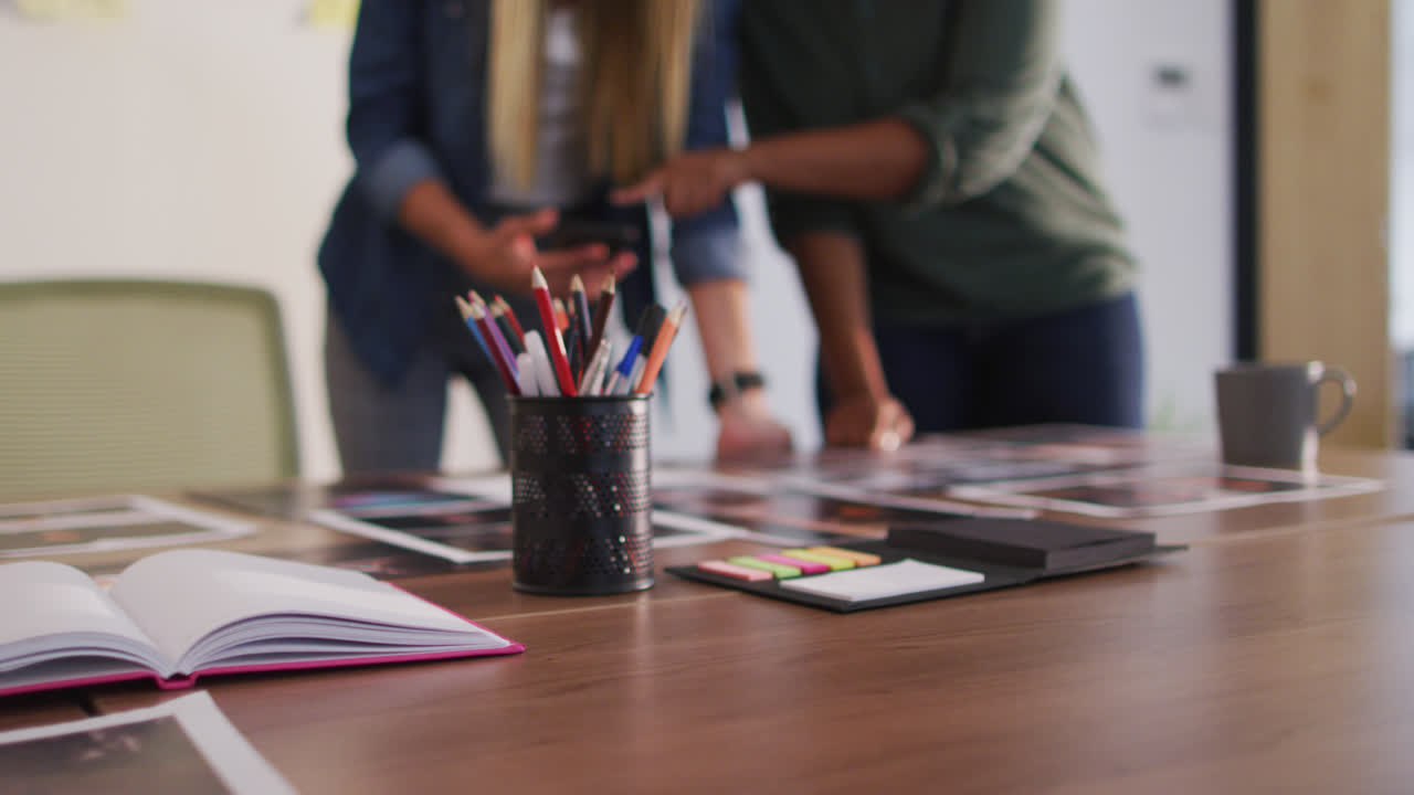 Midsection of two diverse female colleagues looking at smartphone and images standing in office