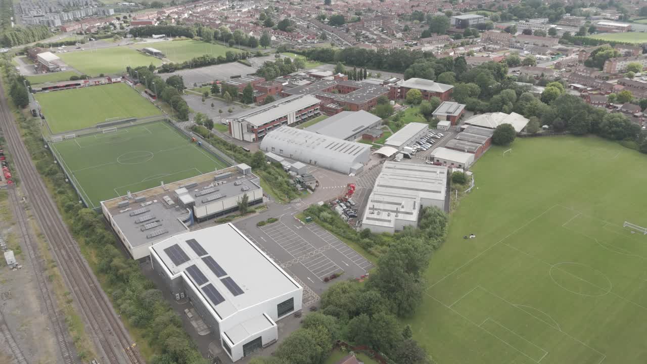 Aerial view of a large campus or sports complex with multiple buildings, sports fields, and adjacent residential areas.