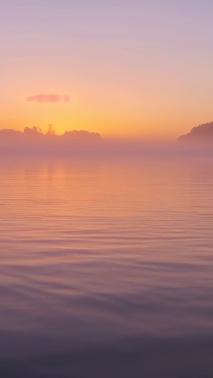 Video verticale: orizzonte che si illumina rivelando il sole che sorge all'alba sull'acqua increspata con la nebbia