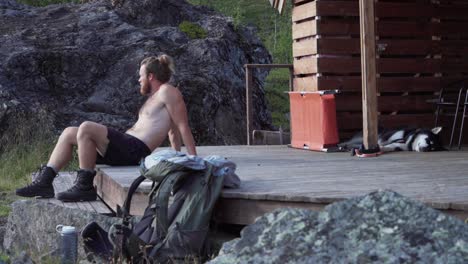 norwegian man half naked looking tired resting on wooden porch of a cottage