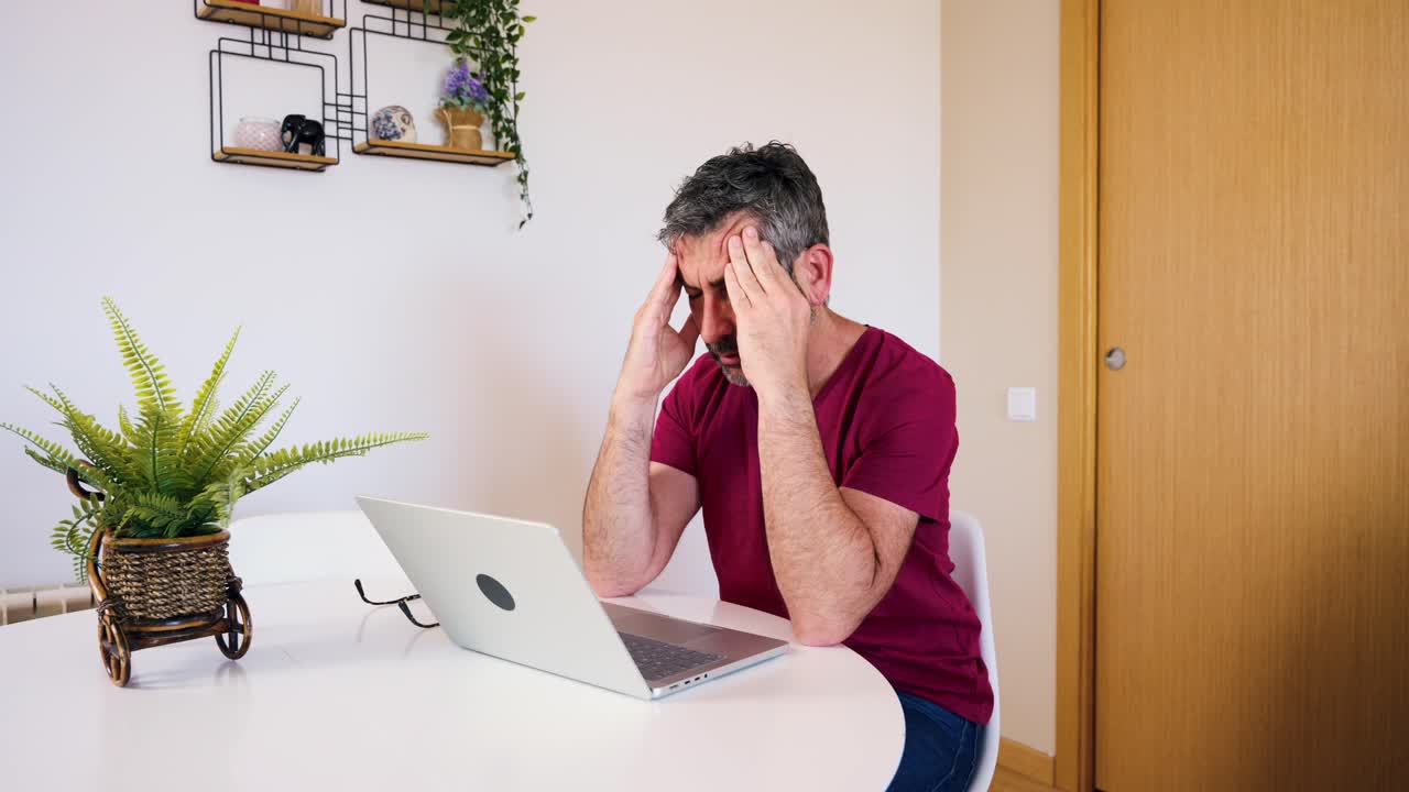 Tired Man Rubbing Eyes While Working on Laptop at Home
