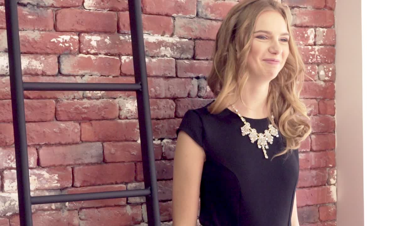 Bright young blond girl is smiling and posing against the brick wall showing v-sign victory or peace