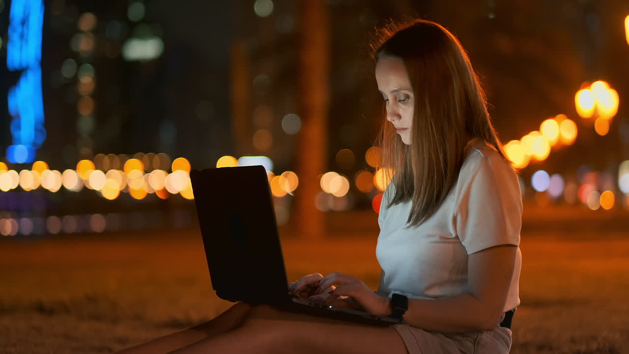 una joven estudiante con una computadora portátil por la noche en la ciudad mirando la pantalla de la computadora y escribiendo con las manos en el teclado. trabajo remoto en internet. la estudiante hace el trabajo. vida nocturna en la ciudad