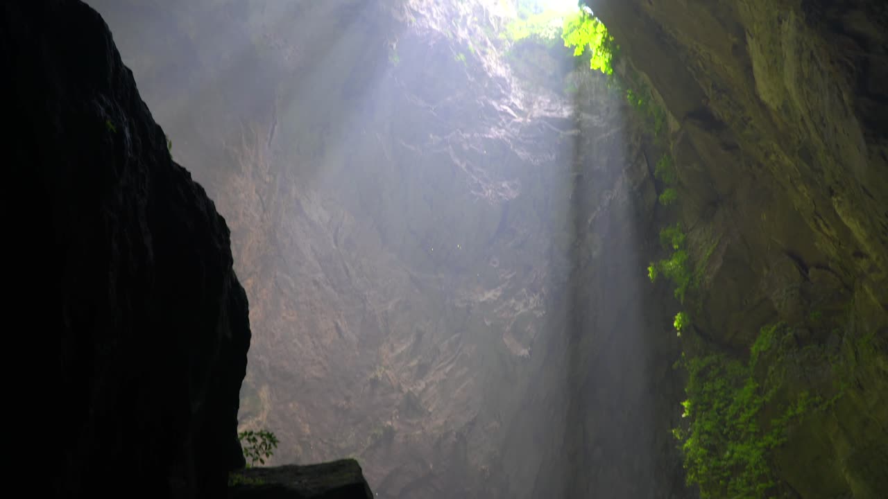 어두운 동굴 내부를 걷고 있는 탐험가에게 햇빛이 비치는 돌리네에서 아래쪽으로 이동합니다.