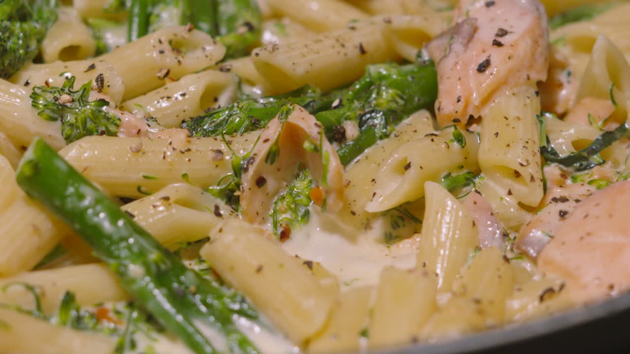 Focus Pull to Bubbling Creamy Delicious Salmon and Broccoli Penne Italian Pasta on Stove with Cracked Black Pepper. Cooking Kitchen Seafood Healthy Eating Footage 4K.