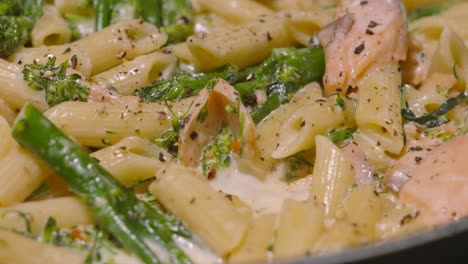 focus pull to bubbling creamy delicious salmon and broccoli penne italian pasta on stove with cracked black pepper. cooking kitchen seafood healthy eating footage 4k.