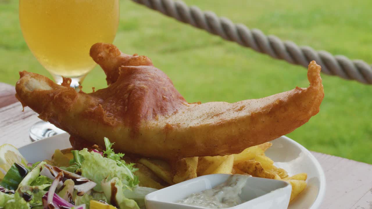 Crispy battered fish, golden fries, fresh salad, and cold beer on a rustic outdoor table