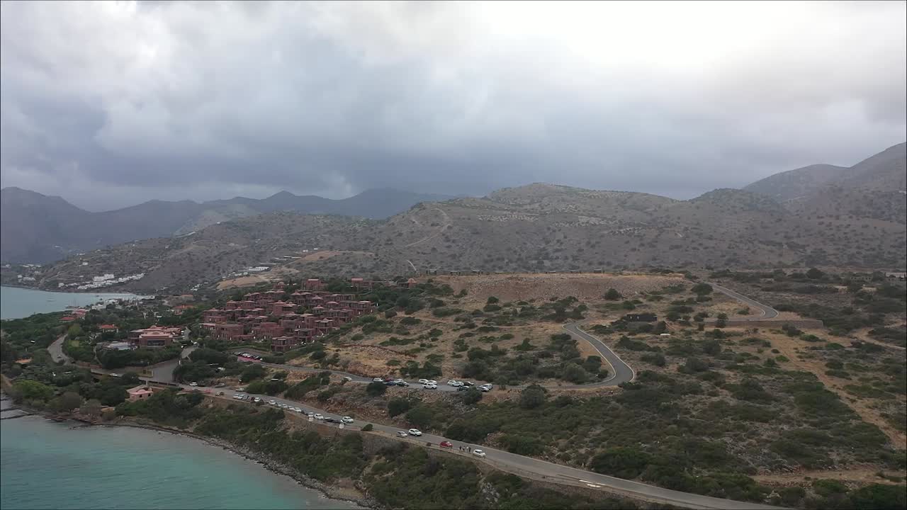 Drone on a journey towards the small mountains with the city in the background, capturing the road where cars are driving near the coast