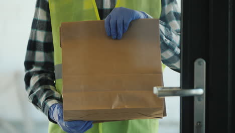un mensajero en guantes con un paquete de comestibles se encuentra fuera de la puerta