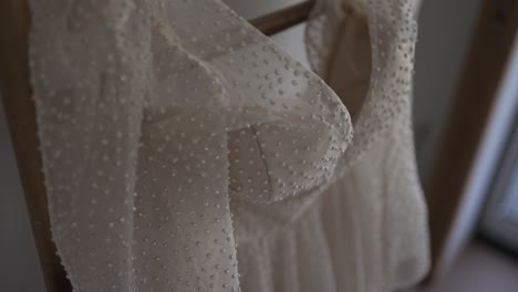 close up of a pearl studded wedding gown draped on a wooden hanger, showcasing intricate details