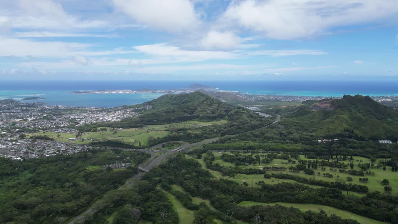 Drone footage showing a panoramic view of Hawaii’s coastline, green mountains, urban areas and cloudy sky.