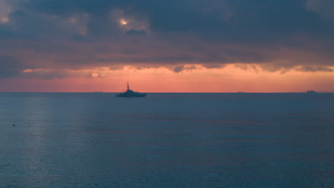 wide aerial view of a royal navy warship sailing on a calm sea at sunrise
