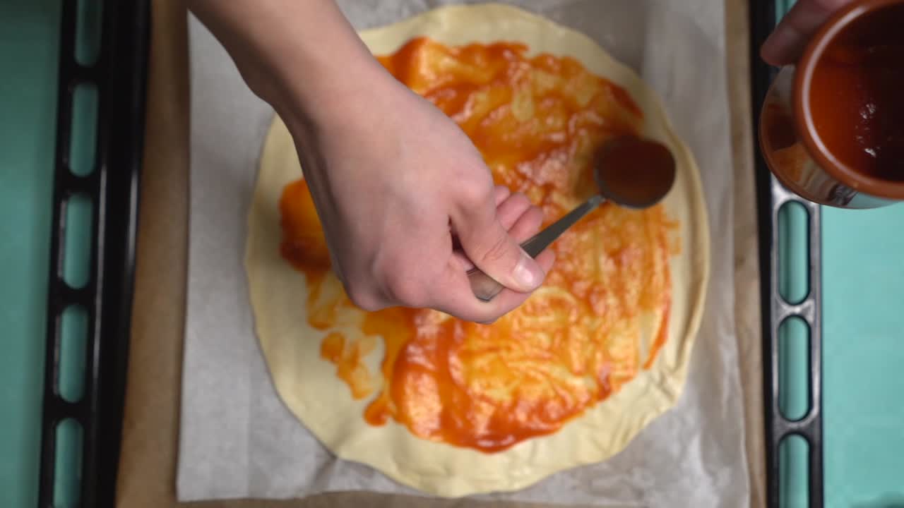 Donna che spalma il pomodoro sull'impasto della pizza creando cerchi con un cucchiaio, ripresa dall'alto.