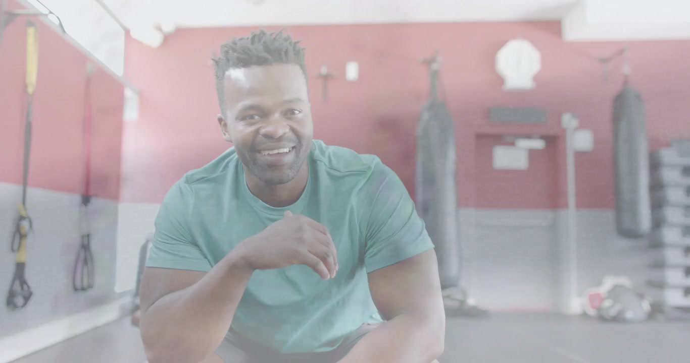 Vertical video: Leaning man in teal shirt reacting to camera rolling, coaching at gym with bags